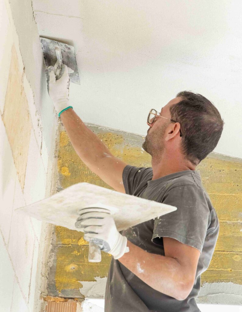 Craftsman in dirty gloves and gray shirt spreading plaster with a metal float over a ceiling